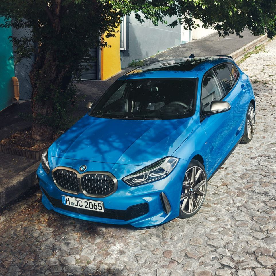 BMW Série 1 au bord de la route. La BMW Série 1 en Misano Blau metallic, vue de trois quarts avant en plongée, en stationnement sur le bord de la route.