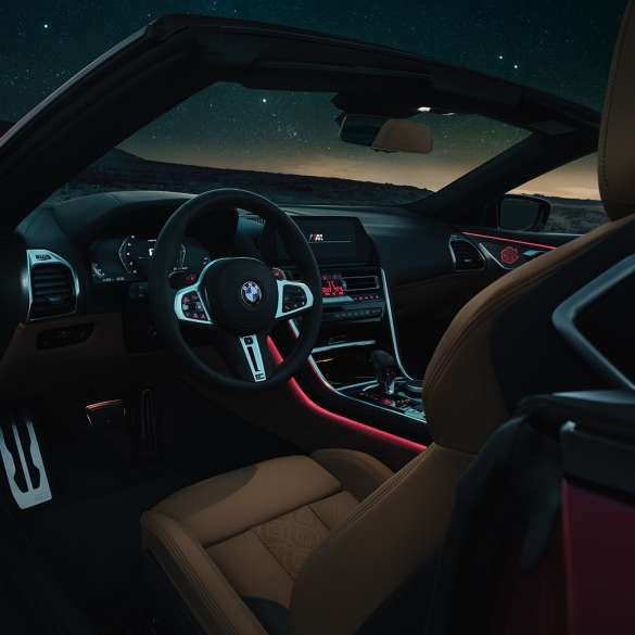 BMW M8 Competition Cabrio, poste de conduite. BMW M8 Competition Cabrio, poste de conduite de nuit avec volant M en cuir et éclairage d’ambiance rouge.