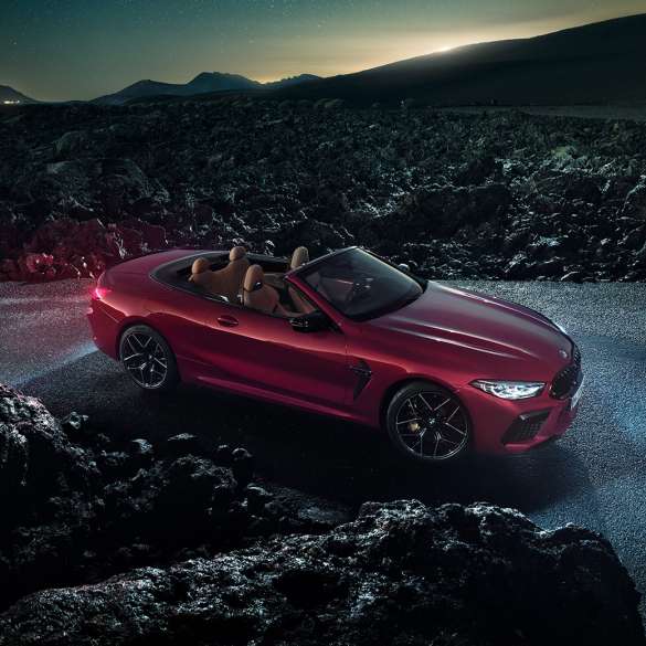 BMW M8 Competition Cabrio, vue de trois quarts de profil. BMW M8 Competition Cabrio en Motegi Rot metallic avec capote ouverte, vue de trois quarts de profil, à l’arrêt sur l’asphalte pendant la nuit.