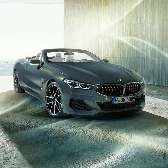 BMW M850i xDrive Cabrio, vue de trois quarts avant. BMW M850i xDrive Cabrio en Dravitgrau metallic avec capote ouverte, vue de trois quarts avant, à l’arrêt devant le littoral.
