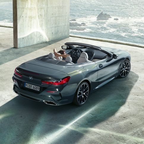 BMW M850i xDrive Cabrio, vue en plongée. BMW M850i xDrive Cabrio en Dravitgrau metallic avec capote ouverte, vue en plongée, en stationnement dans un bâtiment en béton devant l’océan.