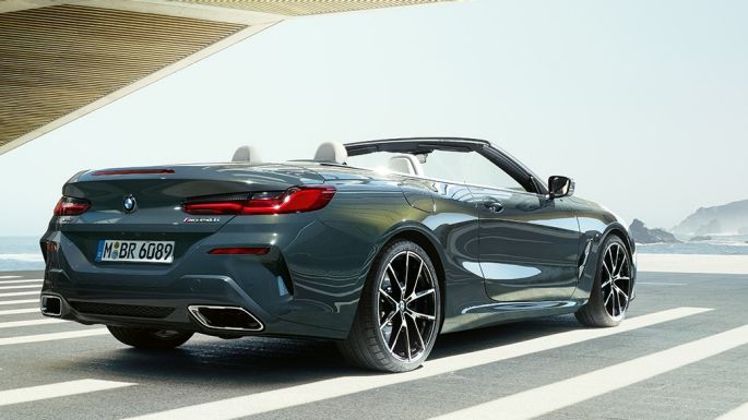 BMW M850i xDrive Cabrio, vue de trois quarts arrière. BMW M850i xDrive Cabrio en Dravitgrau metallic avec capote ouverte, vue de trois quarts arrière, en stationnement avec vue sur l’océan.