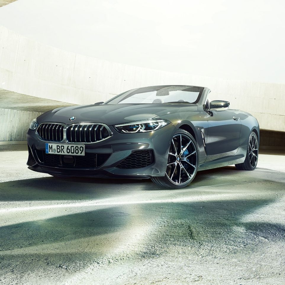 BMW M850i xDrive Cabrio, vue de trois quarts avant. BMW M850i xDrive Cabrio en Dravitgrau metallic avec capote ouverte, vue de trois quarts avant, à l’arrêt dans un bâtiment en béton.