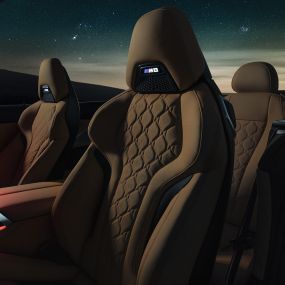Siège M sport en cuir Merino. BMW M8 Competition Cabrio avec capote ouverte sous un ciel étoilé, habitacle avec sièges M sport en cuir Merino et éclairage d’ambiance rouge.