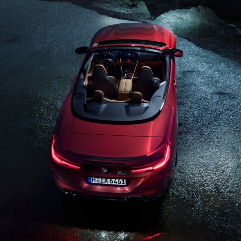 BMW M8 Competition Cabrio, vue en plongée. BMW M8 Competition Cabrio en Motegi Rot metallic avec capote ouverte, à l’arrêt sur l’asphalte, vue en plongée nocturne.