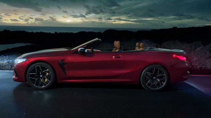 BMW M8 Competition Cabrio, vue de profil. BMW M8 Competition Cabrio en Motegi Rot metallic avec capote ouverte, vue de profil nocturne sous un ciel étoilé.