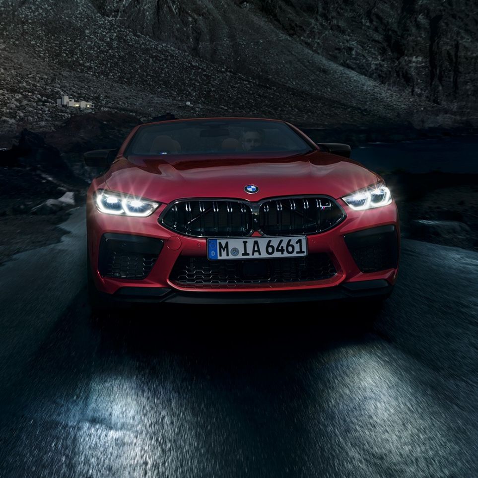 BMW M8 Competition Cabrio, vue avant. BMW M8 Competition Cabrio en Motegi Rot metallic avec phares allumés, vue avant, en conduite de nuit.