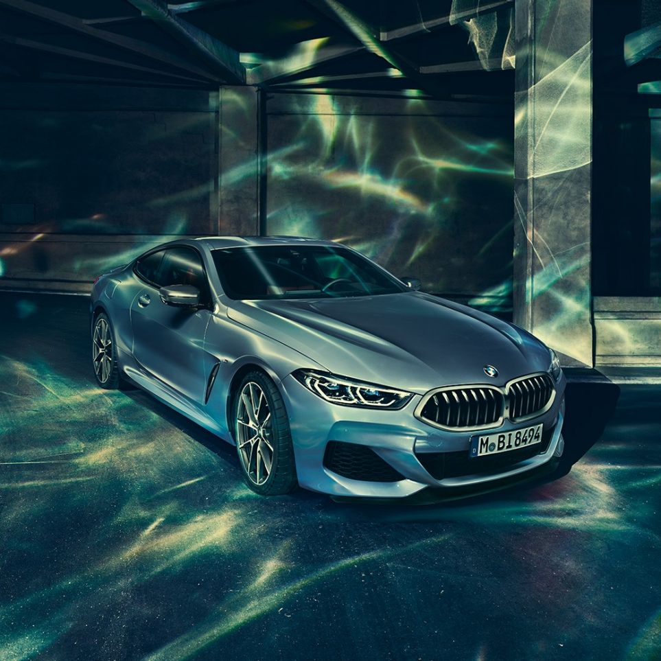 BMW M850i xDrive Coupé, vue de trois quarts avant gauche. BMW M850i xDrive Coupé en Barcelona Blau metallic, vue de trois quarts avant gauche, à l’arrêt devant un immeuble.