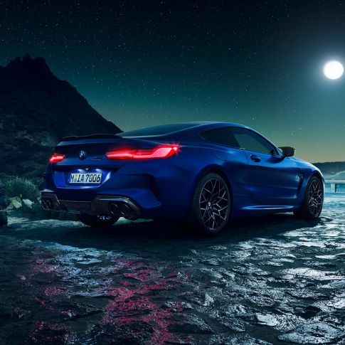 BMW M8 Competition, vue de trois quarts arrière. BMW M8 Competition Coupé en Marina Bay Blau metallic avec feux arrière LED allumés, vue de trois quarts arrière à l’arrêt, sous la pleine lune.