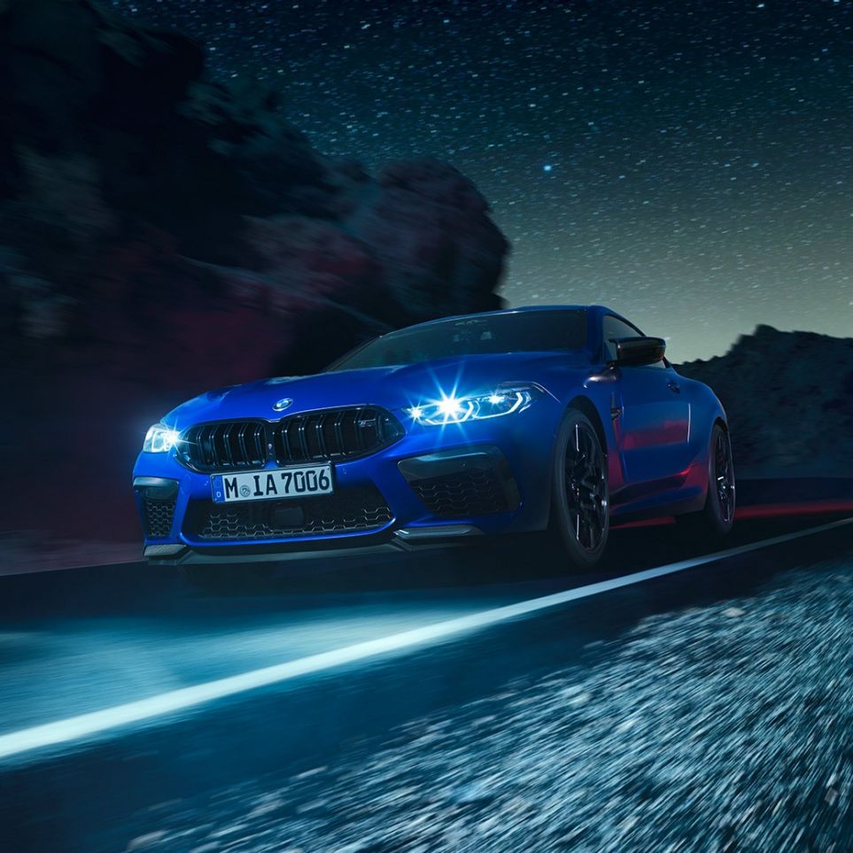 BMW M8 Competition Coupé en marche, vue de trois quarts avant. BMW M8 Competition Coupé en Marina Bay Blau metallic avec phares LED allumés, vue de trois quarts avant en marche, de nuit.