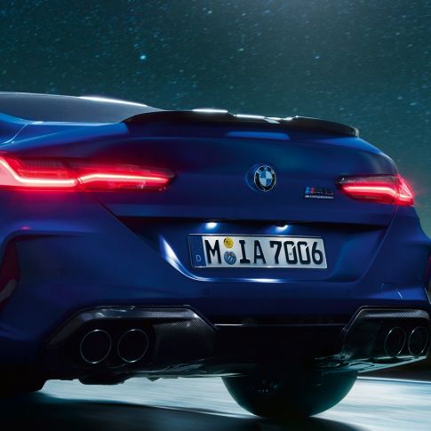 Diffuseur M en Carbon Schwarz. BMW M8 Competition Coupé en Marina Bay Blau metallic, vue en gros plan de la poupe de nuit, avec diffuseur M en Carbon Schwarz.