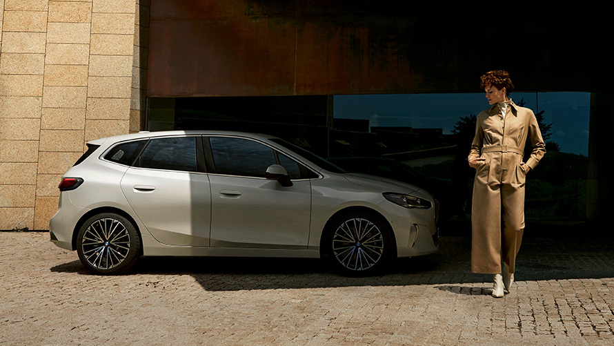 BMW Série 2 Active Tourer U06 2021, vue de côté et mannequin femme BMW Série 2 Active Tourer U06 2021 Mineralweiß métallisé en stationnement, vue de côté et mannequin femme