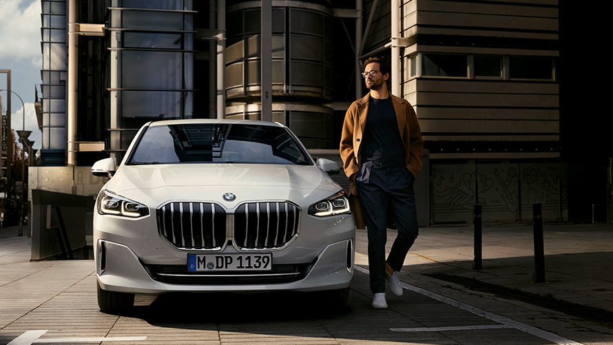 BMW Série 2 Active Tourer U06 2021 - vue de face avec mannequin homme BMW Série 2 Active Tourer U06 2021 Mineralweiß métallisé en stationnement, vue de face avec mannequin homme