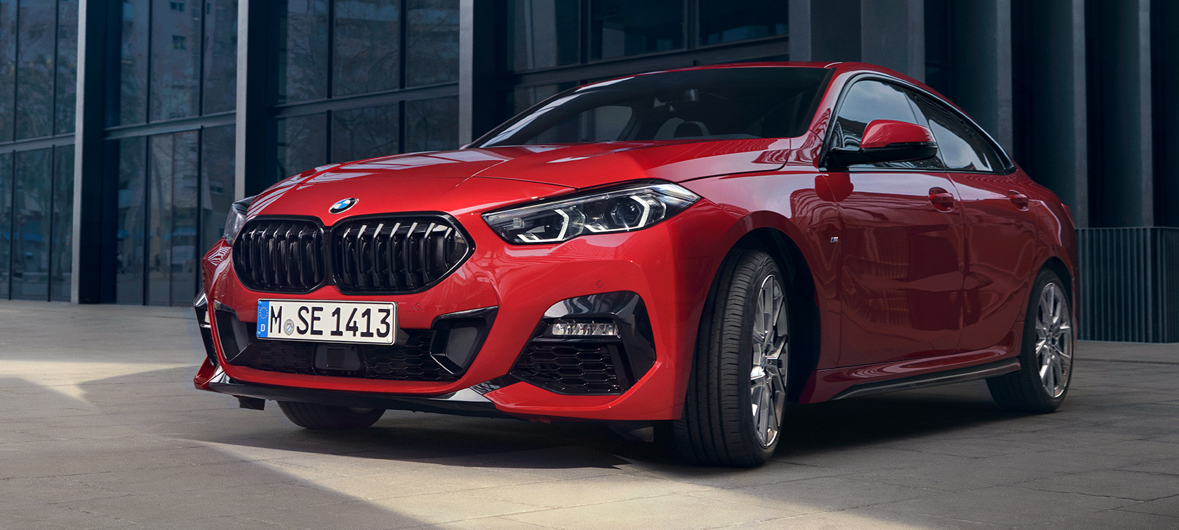 BMW Série 2 Gran Coupé F44 M135i, vue de trois quarts avant Edition ColorVision Melbourne Rot metallic devant un bâtiment
