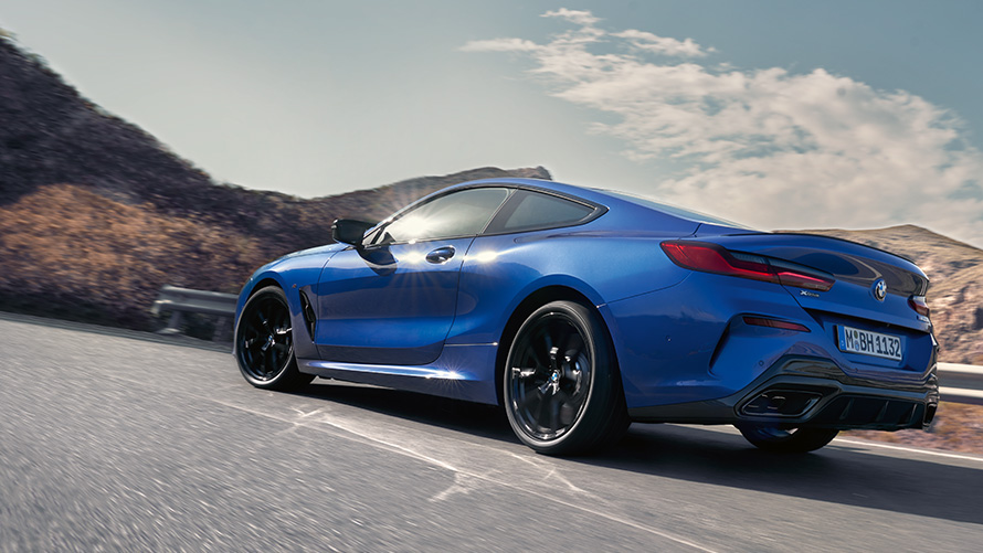 La nouvelle BMW Série 8 Coupé M Portimao Blau metallic G15 LCI restylage vue de trois quarts arrière face aux collines