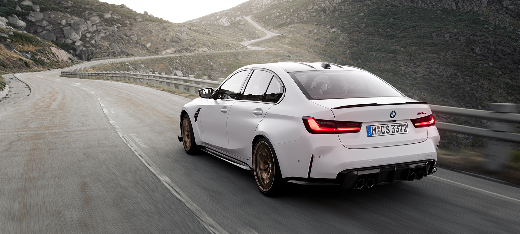 BMW M3 CS G80 vue de trois quarts arrière en mouvement sur une route en montagne