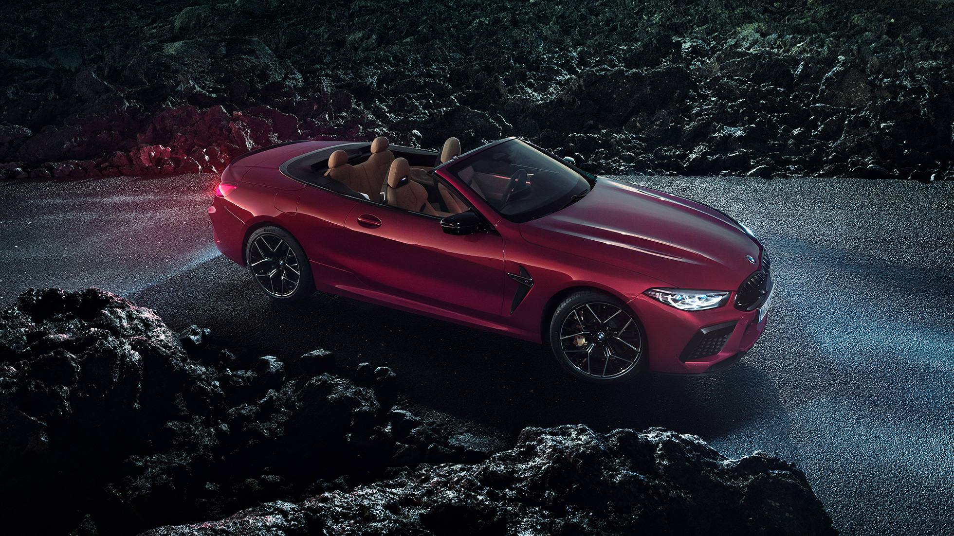 BMW M8 Competition Cabrio, vue de trois quarts de profil. BMW M8 Competition Cabrio en Motegi Rot metallic avec capote ouverte, vue de trois quarts de profil, à l’arrêt sur l’asphalte pendant la nuit.