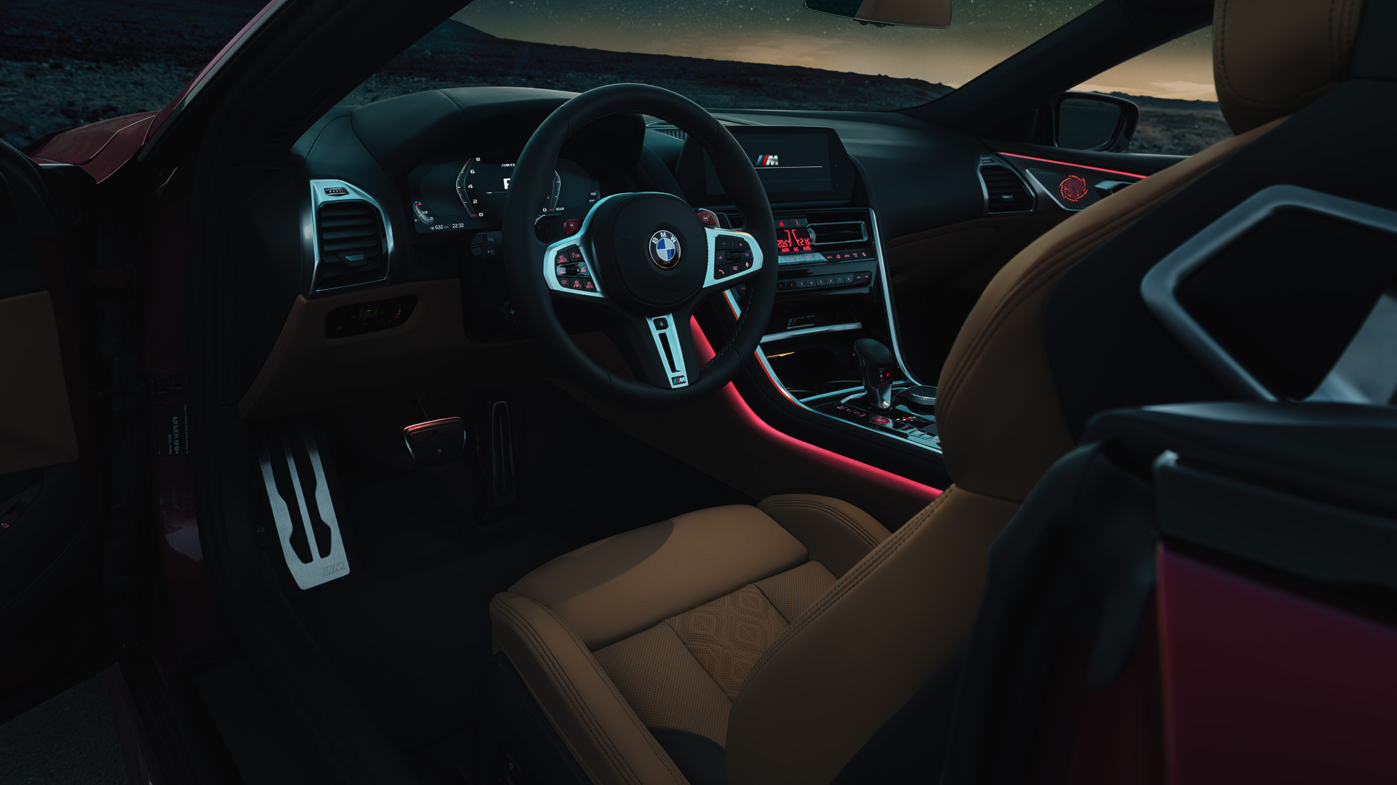 BMW M8 Competition Cabrio, poste de conduite. BMW M8 Competition Cabrio, poste de conduite de nuit avec volant M en cuir et éclairage d’ambiance rouge.