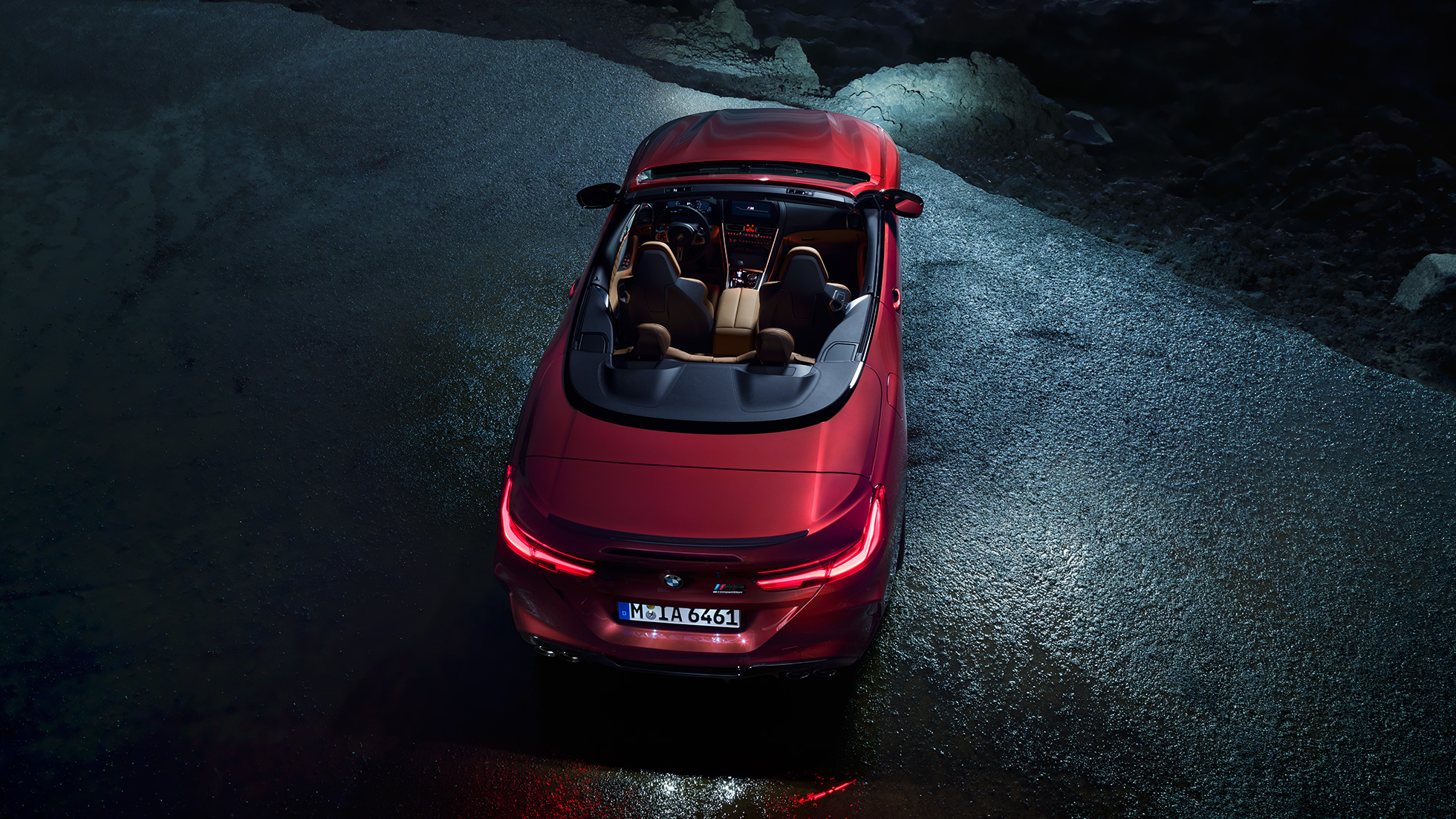 BMW M8 Competition Cabrio, vue en plongée. BMW M8 Competition Cabrio en Motegi Rot metallic avec capote ouverte, à l’arrêt sur l’asphalte, vue en plongée nocturne.