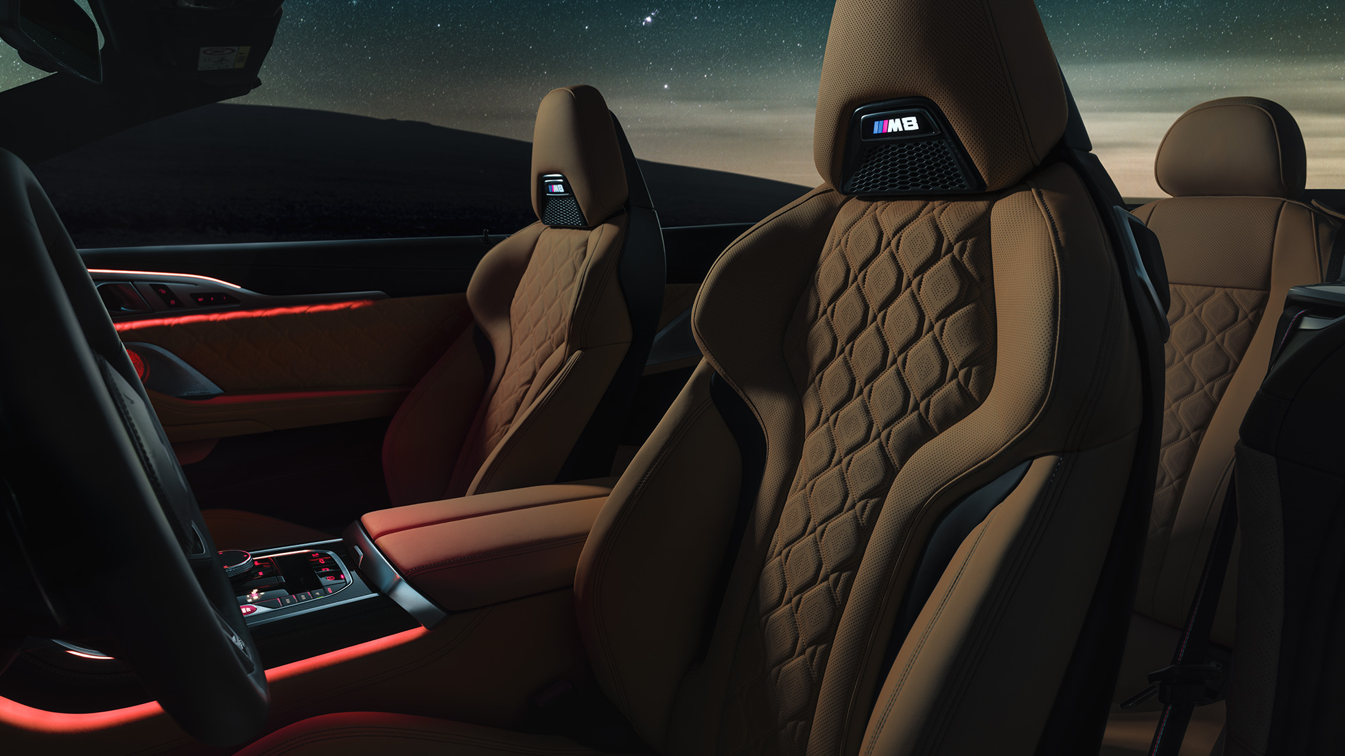 Siège M sport en cuir Merino. BMW M8 Competition Cabrio avec capote ouverte sous un ciel étoilé, habitacle avec sièges M sport en cuir Merino et éclairage d’ambiance rouge.