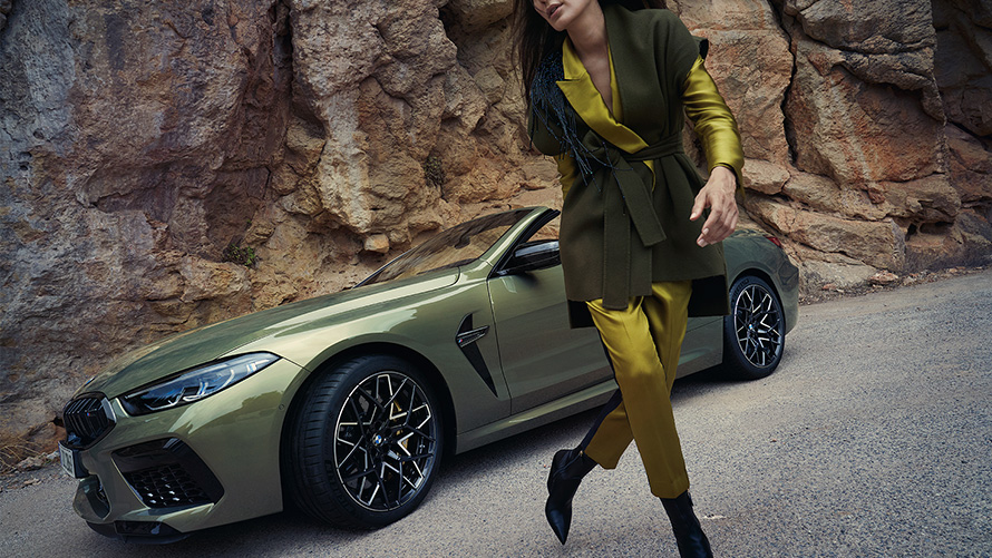 La nouvelle BMW M8 Competition Cabrio F91 LCI restylage 2022 BMW Individual Brass metallic vue de trois quarts avant sur un terrain rocailleux avec mannequin féminin