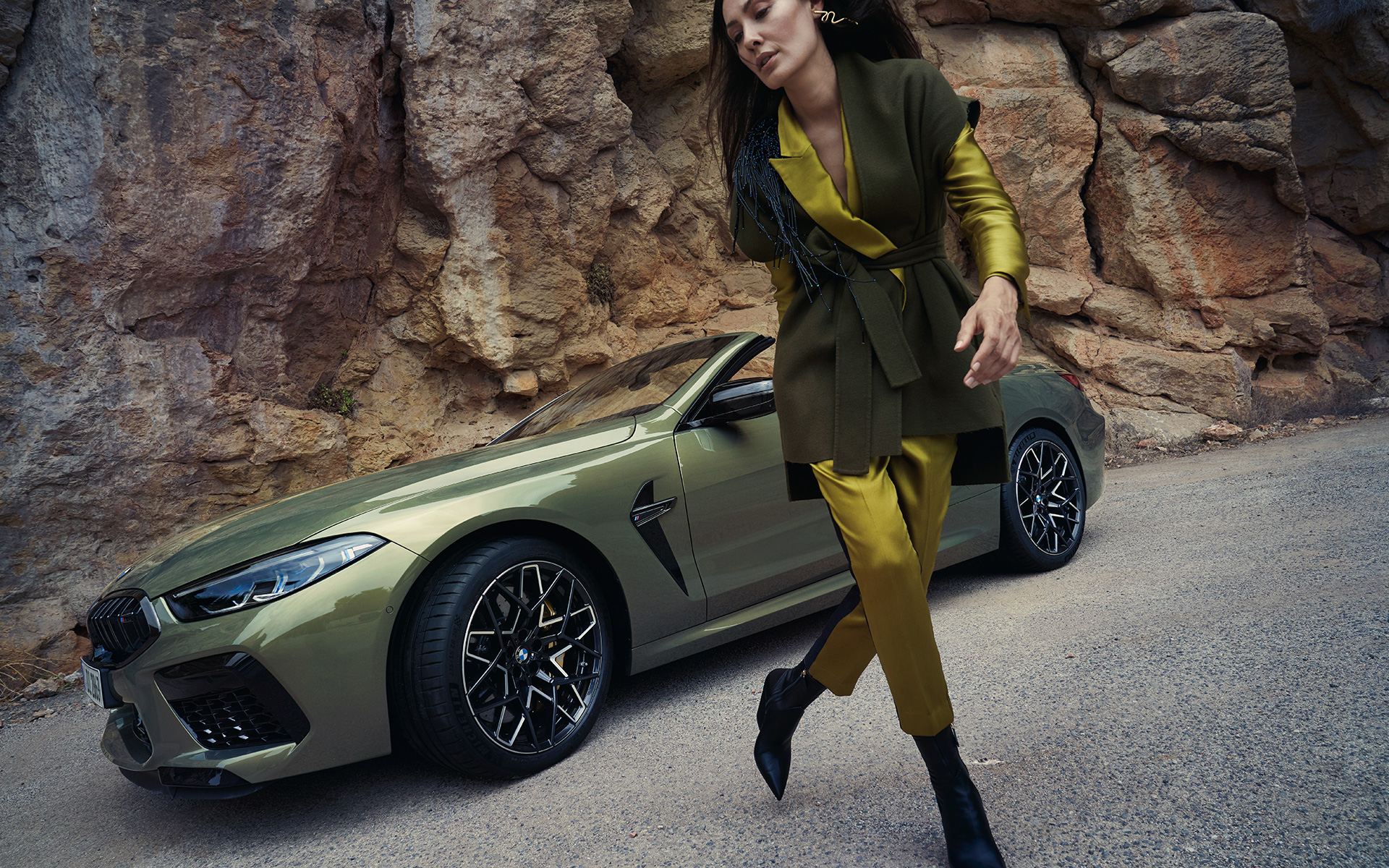 La nouvelle BMW M8 Competition Cabrio F91 LCI restylage 2022 BMW Individual Brass metallic vue de trois quarts avant sur un terrain rocailleux avec mannequin féminin