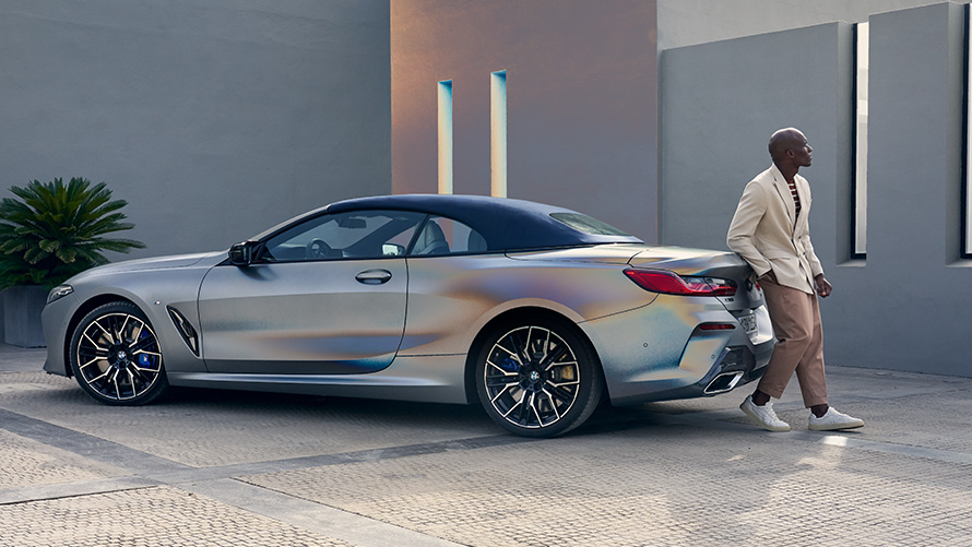 La nouvelle BMW M850i xDrive Cabrio G14 LCI restylage 2022 BMW Individual Frozen Pure Grey metallic, vue de trois quarts arrière adossée au véhicule avec un modèle homme
