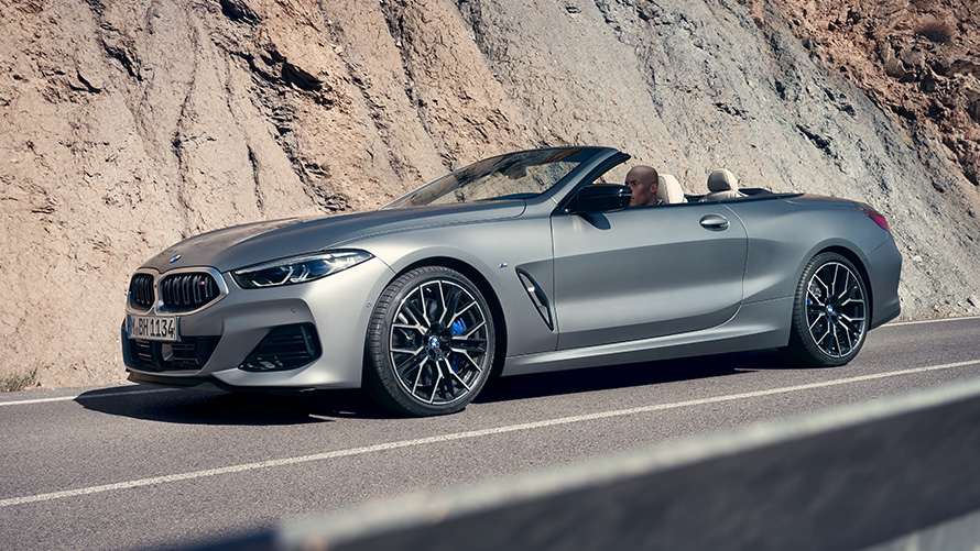 La nouvelle BMW M850i xDrive Cabrio G14 LCI restylage 2022 BMW Individual Frozen Pure Grey metallic, vue de trois quarts avant en mouvement devant des roches