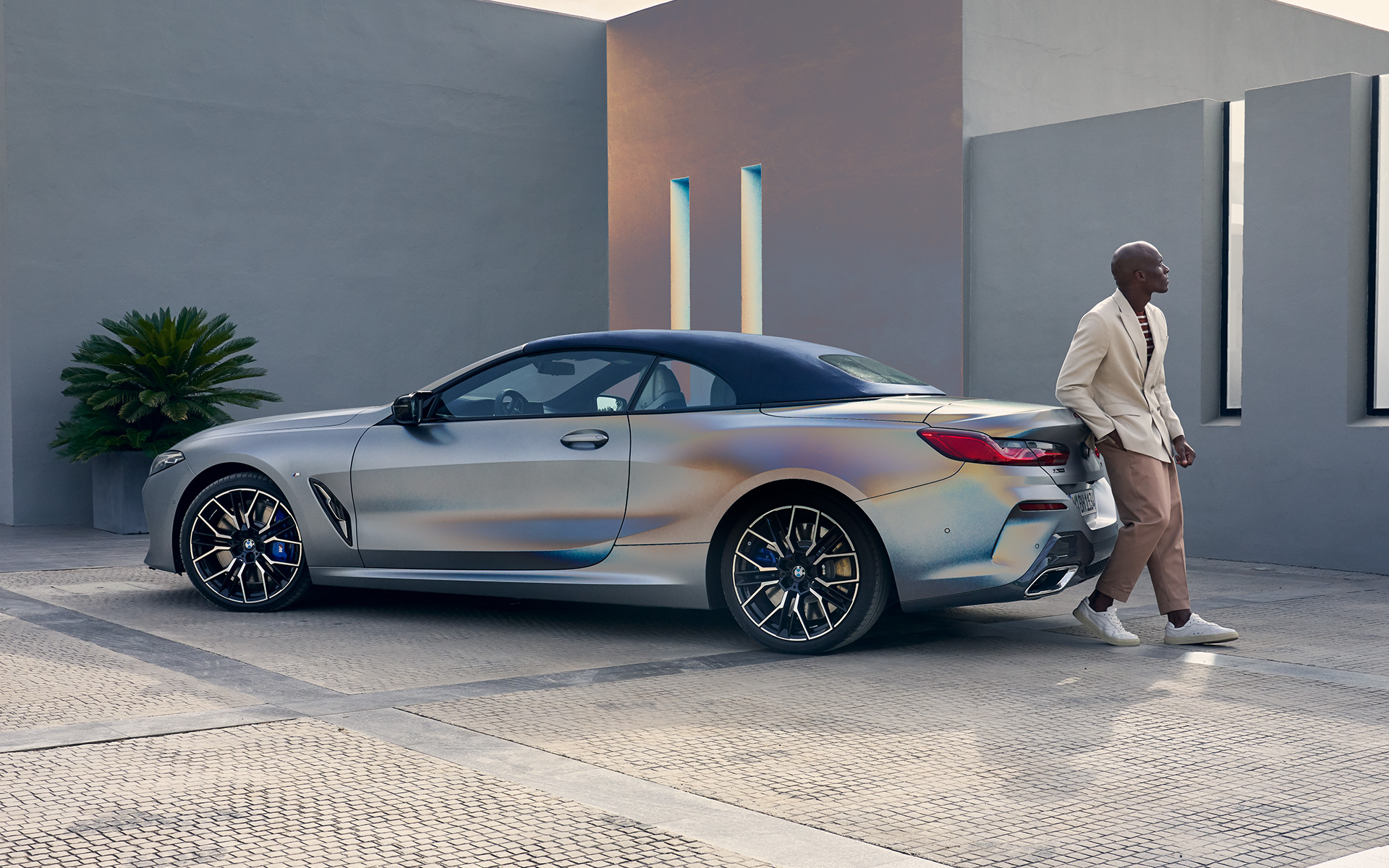 La nouvelle BMW M850i xDrive Cabrio G14 LCI restylage 2022 BMW Individual Frozen Pure Grey metallic, vue de trois quarts arrière adossée au véhicule avec un modèle homme