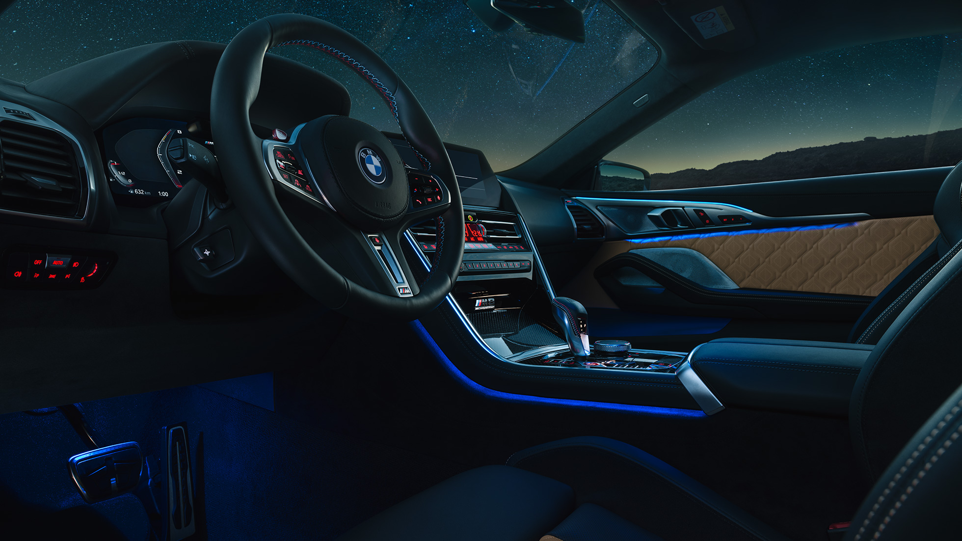 BMW M8 Competition Coupé, poste de conduite. BMW M8 Competition Coupé, prise de vue nocturne du poste de conduite avec volant M en cuir et éclairage d’ambiance bleu.