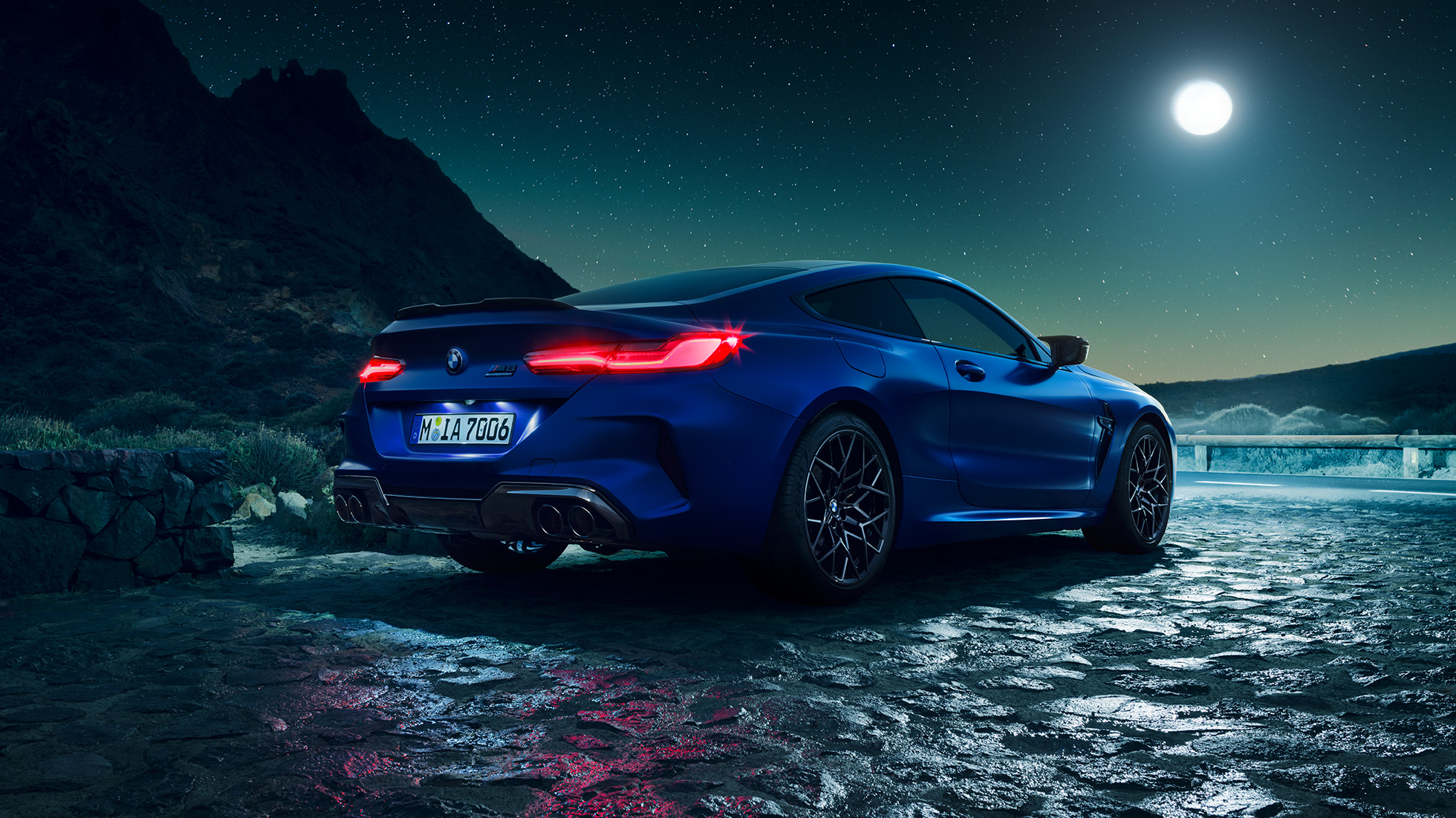 BMW M8 Competition, vue de trois quarts arrière. BMW M8 Competition Coupé en Marina Bay Blau metallic avec feux arrière LED allumés, vue de trois quarts arrière à l’arrêt, sous la pleine lune.