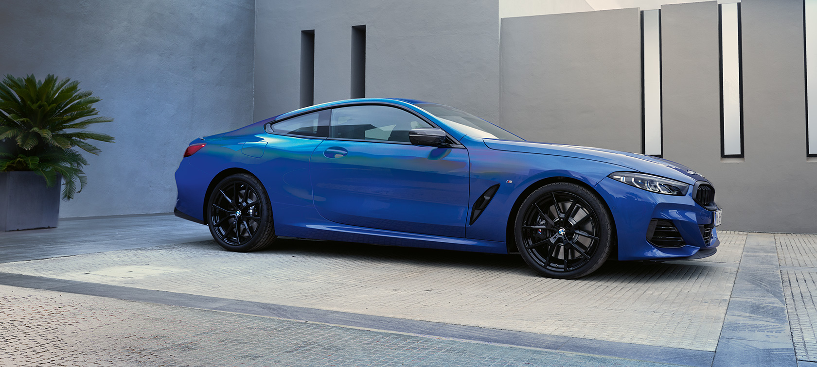 La BMW M850i xDrive Coupé G15 LCI restylage 2022 M Portimao Blau metallic Vue latérale avant en stationnement devant bâtiment