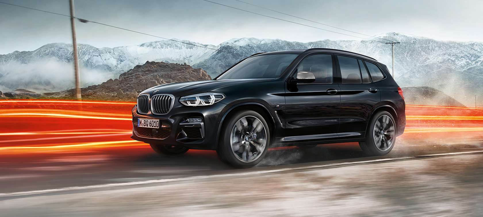BMW X3 M40i et BMW X3 M40d, vue de profil. Extérieur des BMW X3 M40i et BMW X3 M40d en Saphierschwarz metallic, en mouvement, vue de profil devant un paysage montagneux avec bandes lumineuses.