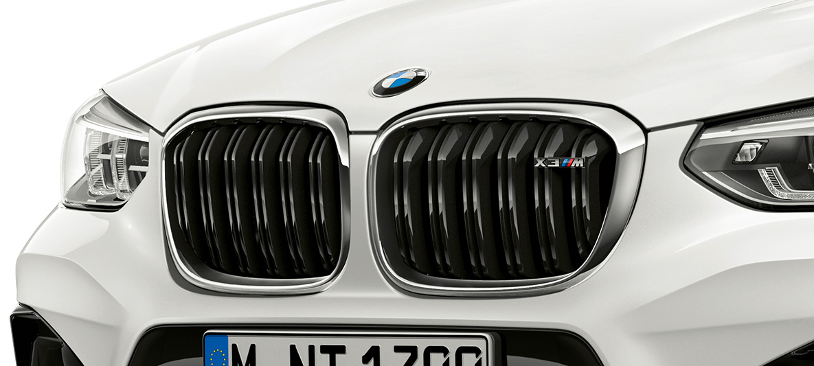 BMW X3 M, naseaux M. Extérieur de la BMW X3 M en Alpinweiß, avant, naseaux M avec accents chromés et insigne du modèle.