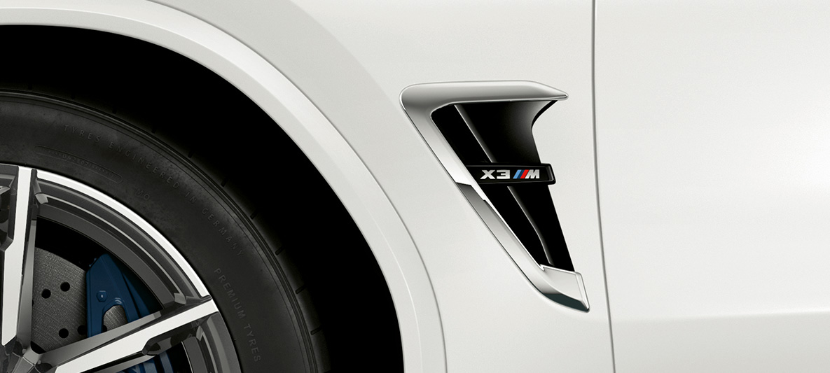 BMW X3 M, naseaux M. Extérieur de la BMW X3 M en Alpinweiß, avant, naseaux M avec accents chromés et insigne du modèle.