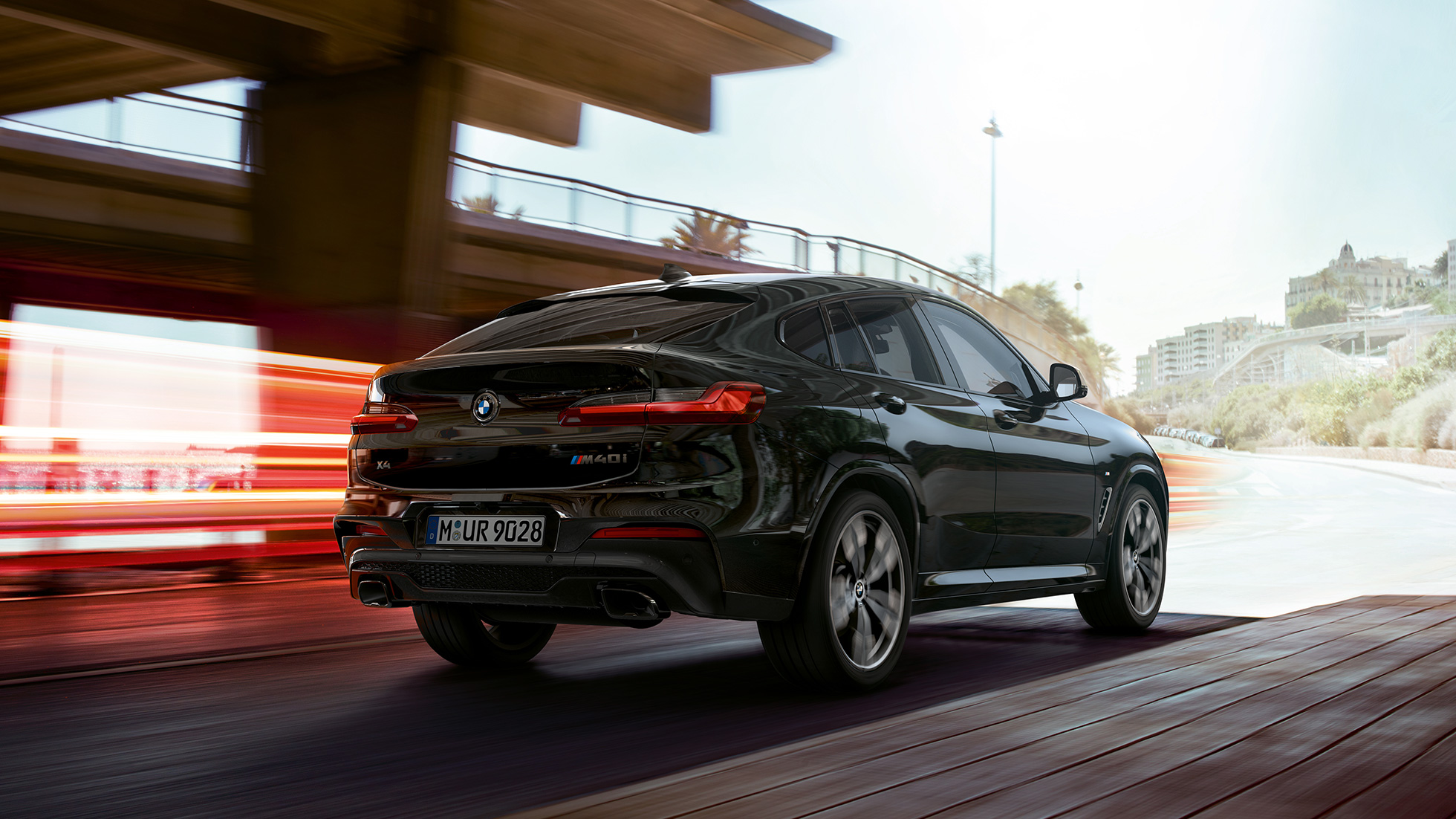 BMW X4 M40i, vue de trois quarts avant. Extérieur de la BMW X4 M40i en Saphierschwarz metallic, en mouvement, vue de trois quarts avant avec bandes lumineuses.