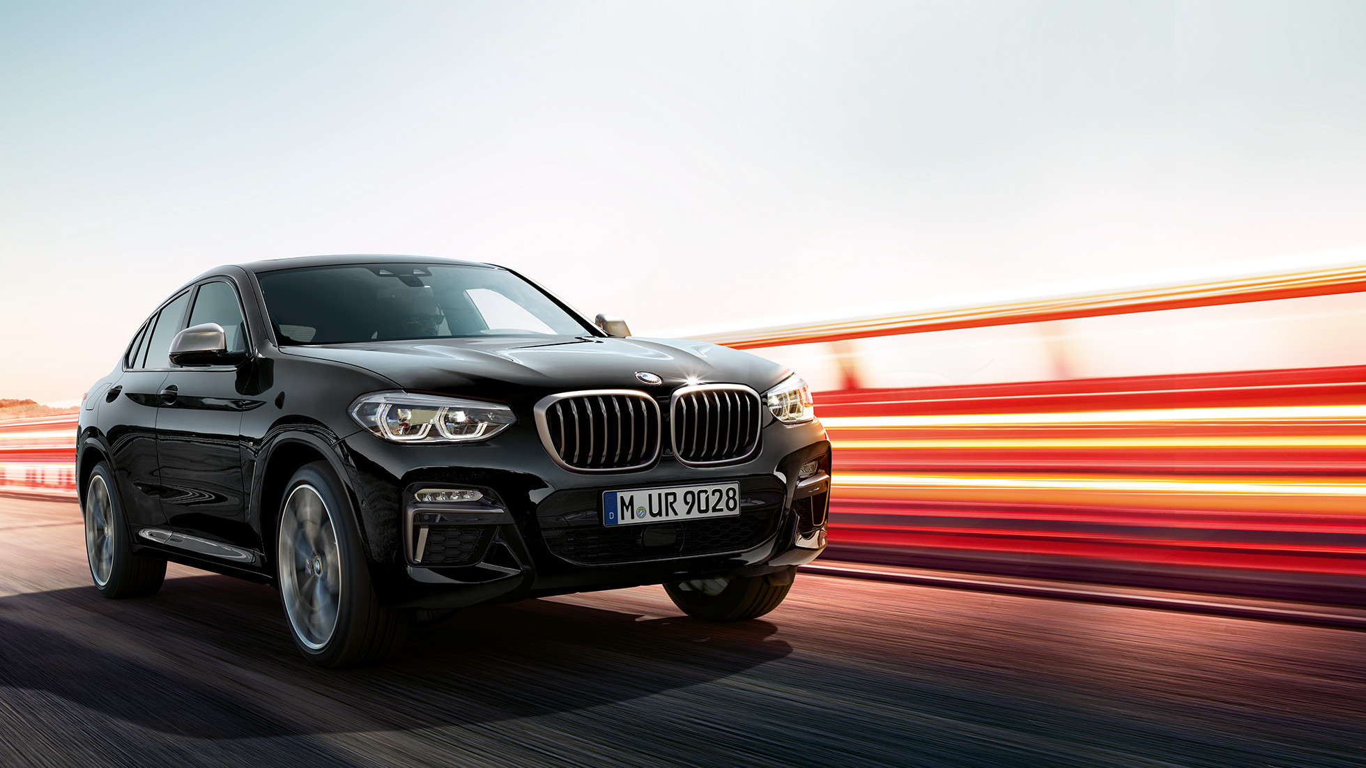 BMW X4 M40i, vue de trois quarts arrière. Extérieur de la BMW X4 M40i en Saphierschwarz metallic, en mouvement, vue de trois quarts arrière avec bandes lumineuses.
