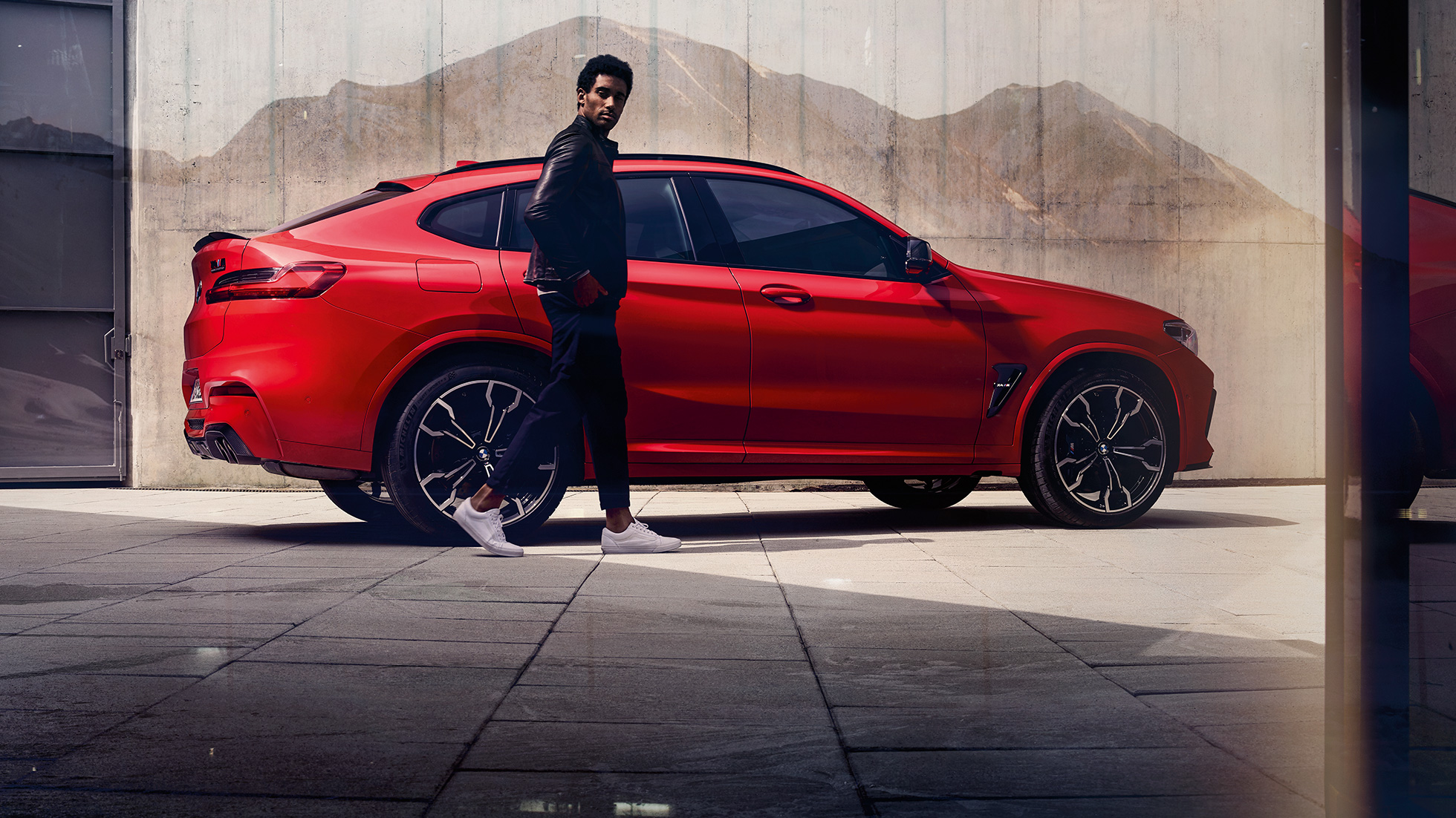 BMW X4 M Competition, vue de profil avec jeune homme. Extérieur de la BMW X4 M Competition en Toronto Rot metallic, vue de profil avec jeune homme.