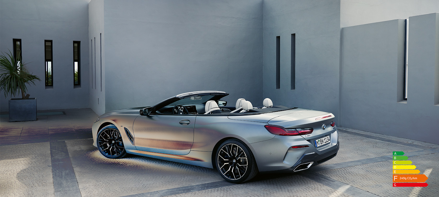 Homme appuyé sur une BMW Série 8 Cabrio G14 LCI restylage 2022 BMW Individual BMW Individual Frozen Pure Grey metallic, vue de profil, devant un bâtiment
