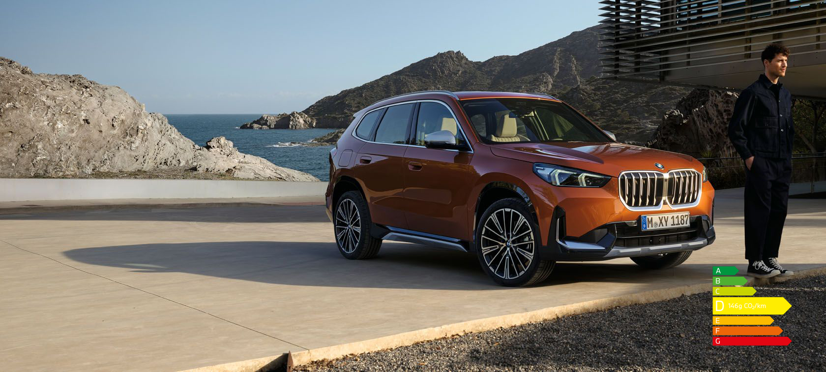BMW X1 U11 xLine Utah orange metallic, vue de trois quarts avant sur route de campagne